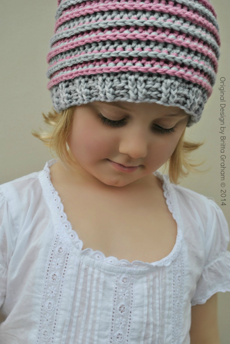 May include: A young girl wearing a gray and pink striped knitted hat. The hat has a simple design with alternating stripes of gray and pink yarn.