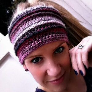 Peut inclure: Une femme portant un bandeau crocheté rayé violet, rose et blanc. Le bandeau est porté sur le front et couvre les oreilles.