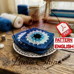 Puede incluir: Una pila de cuadrados de ganchillo azules y blancos con un diseño negro central, sobre un plato decorativo plateado. La imagen incluye carretes de hilo, un dedal y un patrón PDF etiquetado "PATTERN ENGLISH".