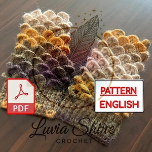 Op de afbeelding: Close-up van een haakpatroon met een schubbenachtig ontwerp in tinten bruin, beige en paars. De afbeelding bevat een PDF-pictogram en de tekst "PATTERN ENGLISH". Het Luvia Shine Crochet-logo is ook zichtbaar.