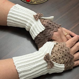 May include: Crocheted fingerless gloves in cream and brown. The cream-colored wrist cuffs have a ribbed texture and small brown bows. The open-palm section is a brown, lacy crochet design.