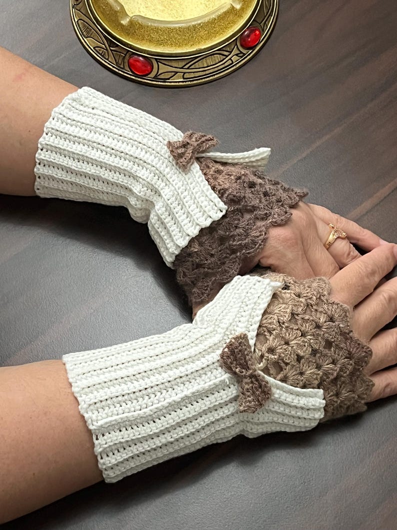 May include: Crocheted fingerless gloves in cream and brown. The cream-colored wrist cuffs have a ribbed texture and small brown bows. The open-palm section is a brown, lacy crochet design.