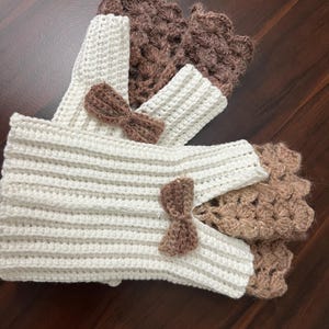 May include: Crocheted fingerless gloves and wrist warmers in cream and brown. The cream-colored gloves have a ribbed design and are adorned with small brown bows. The brown wrist warmers have a textured, openwork pattern.