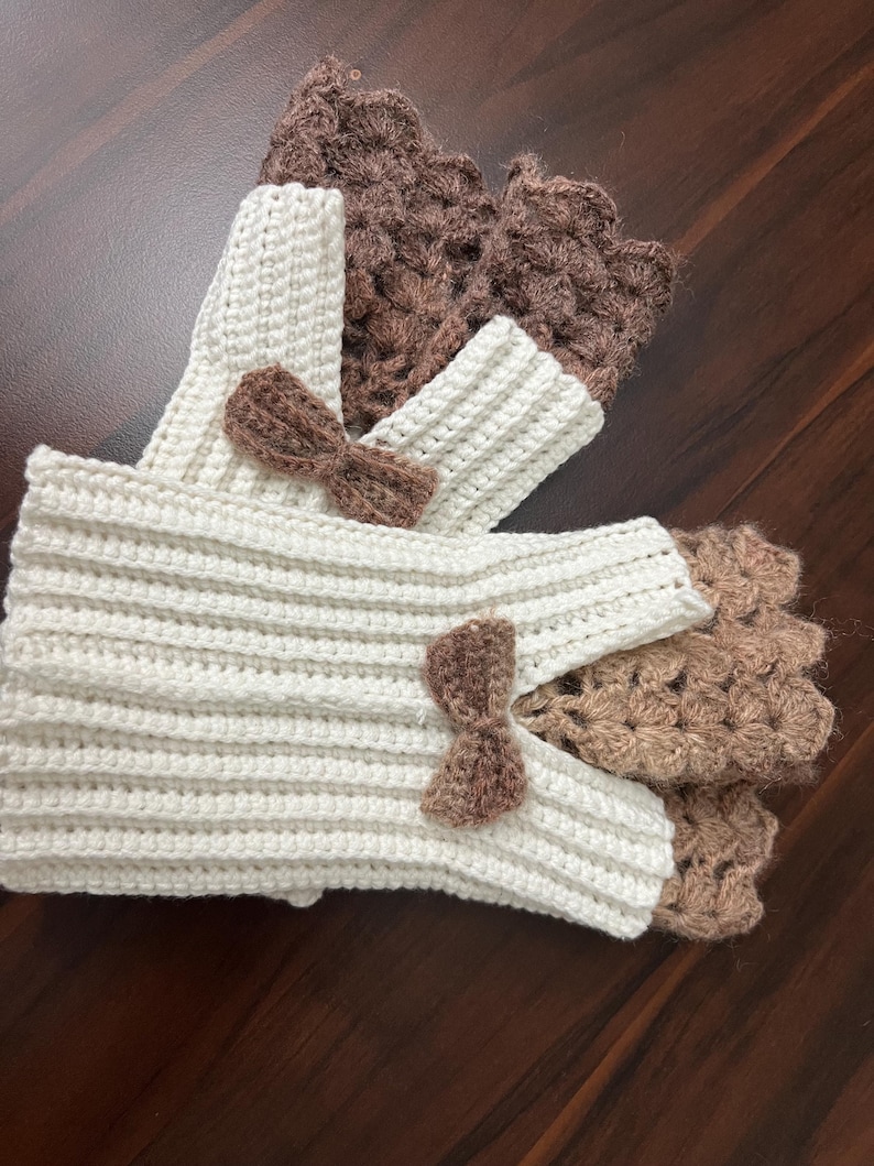 May include: Crocheted fingerless gloves and wrist warmers in cream and brown. The cream-colored gloves have a ribbed design and are adorned with small brown bows. The brown wrist warmers have a textured, openwork pattern.