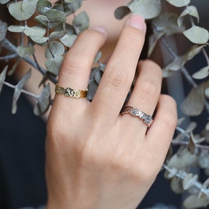 May include: Two gold rings with a textured design. The rings are worn on the finger of a person's hand.