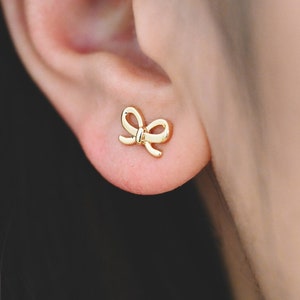 May include: Gold bow-shaped stud earrings. The earrings are small and delicate, and they are perfect for adding a touch of elegance to any outfit.