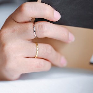 May include: A person's hand wearing two thin gold and silver rings. The hand is holding a book with a barcode on the back cover.