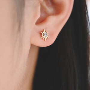 May include: A close-up of a person's ear with a small gold star-shaped earring with a clear stone in the center.