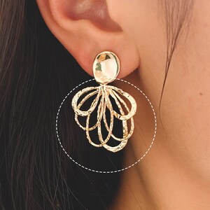 May include: Gold dangle earrings with a textured oval top and a cluster of interconnected circles hanging below.