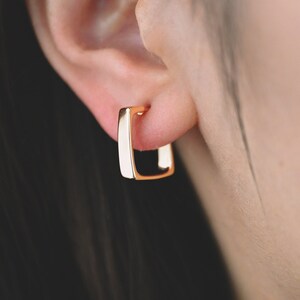 May include: Gold square hoop earrings. The earrings are small and delicate, and they are a simple and elegant design.