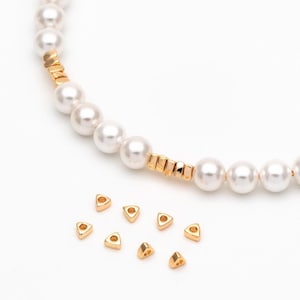 May include: A white pearl necklace with gold spacers and a scattering of small gold triangle beads.