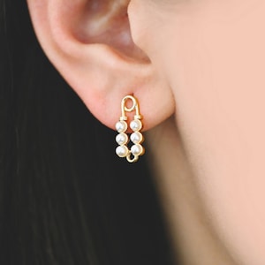 May include: Gold safety pin earrings with a row of small white pearls on each side.