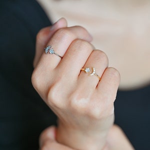 May include: Two gold rings with small clear stones. One ring features a crescent moon design and the other has a cluster of three stones.