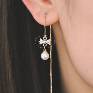Op de afbeelding: Gouden oorhangers met een parel en een klein strikje met heldere strass.
