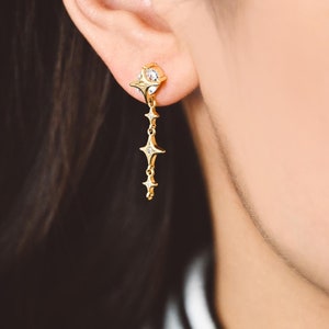 May include: Gold star-shaped earrings with small clear stones. The earrings dangle from a chain with multiple star-shaped charms.