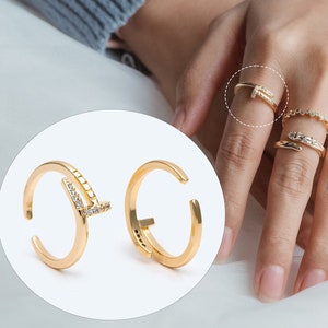 以下が含まれることがあります： ミニマルなデザインのゴールドリング2つ。1つのリングは、小さなクリアストーンがついた直線デザイン、もう1つのリングはシンプルな円形デザインです。