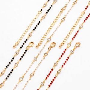 May include: Five gold chains with different colored beads and clear rhinestones. The chains are on a white background.