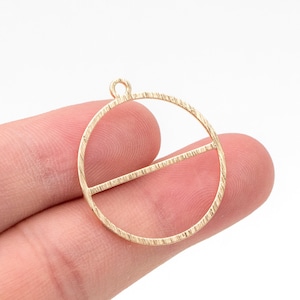 May include: Gold-toned metal circle pendant with a textured surface and a horizontal bar across the center.