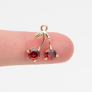 Pode incluir: Encanto de ouro com duas cerejas de cristal vermelho. O encanto tem um design de folha de ouro.