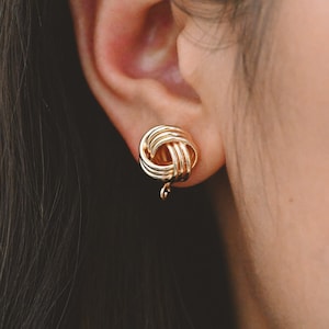 May include: Gold knot-shaped earrings with a dangling loop.