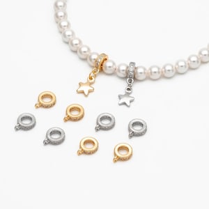 May include: Jewellery charms in gold and silver, some with star pendants. The round charms have attachment rings and are decorated with small, clear stones. A pearl necklace is also present in the image.