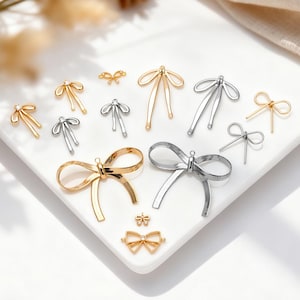 May include: Various gold and silver bow-shaped charms and embellishments are displayed. The charms, in different sizes, are arranged on a white surface. These decorative bows could be used for jewellery making or craft projects. Some have intricate details.