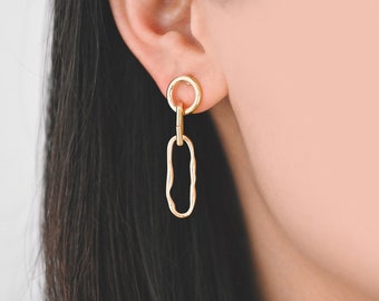 Puede incluir: Pendientes de cadena de oro con un círculo pequeño y un eslabón ovalado más grande. Los pendientes tienen un diseño simple y elegante.