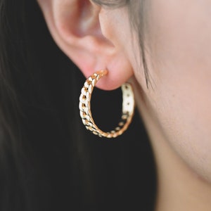 Puede incluir: Pendientes de aro dorados con diseño de cadena.