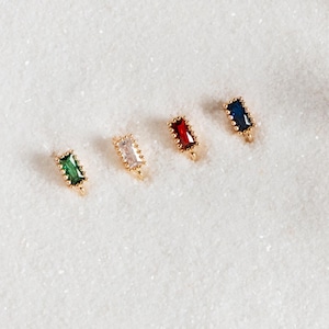 May include: Four gold-toned charms with different colored rectangular stones. The stones are green, white, red, and blue.