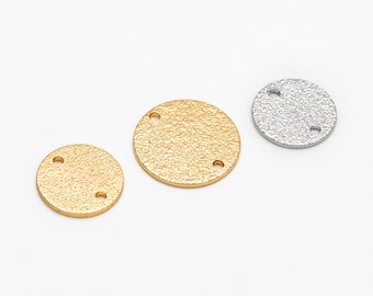 Puede incluir: Tres abalorios redondos de metal texturizado en oro y plata. Cada abalorio tiene dos pequeños agujeros para sujetarlos a otros componentes de joyería. Los abalorios están dispuestos sobre un fondo blanco.