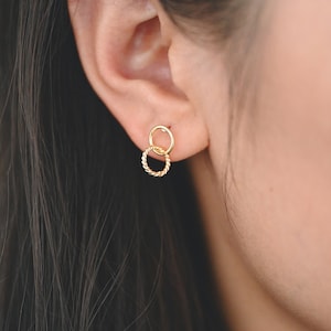 Può includere: Orecchini a cerchio doppio dorati con un design intrecciato. L'anello più piccolo è all'interno del più grande.