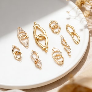 Peut inclure: Une collection de connecteurs et maillons de bijoux dorés de formes variées, incluant des designs ovales, en goutte d'eau et en forme de menottes. Plusieurs pièces présentent des cristaux clairs incrustés, tandis que d'autres ont une finition métallique lisse.