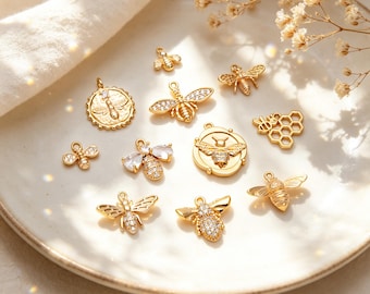May include: A collection of gold-toned bee-themed jewelry charms in various designs, including several bee shapes with clear crystal accents, a honeycomb charm, and two circular coin-style pendants featuring embossed bee motifs.