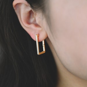 May include: Gold square hoop earrings. The earrings are simple and modern.