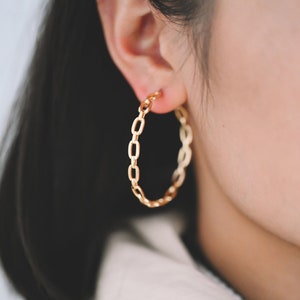 Puede incluir: Pendientes de aro dorados con diseño de cadena.