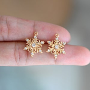 Puede incluir: Dos abalorios de copo de nieve dorados con detalles de cristal transparente. Los abalorios tienen un diseño delicado e intrincado y son perfectos para añadir un toque de brillo a los proyectos de joyería.