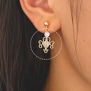 May include: Gold dangle earrings with a clear crystal and a delicate, intricate design.