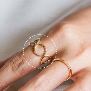 Puede incluir: Anillo de oro con un diseño de círculos entrelazados. El anillo se lleva en un dedo.