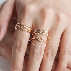 May include: A gold ring with a circle of small stones. The ring is worn on a finger with other gold rings.