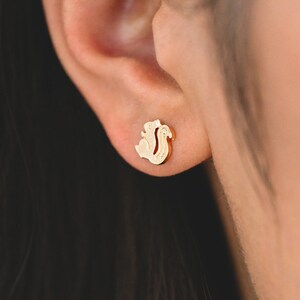 Könnte beinhalten: Nahaufnahme eines Ohrs mit einem kleinen goldenen Eichhörnchen-Ohrstecker.