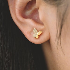 May include: A pair of gold butterfly stud earrings. The earrings are small and delicate, and they are perfect for adding a touch of elegance to any outfit.