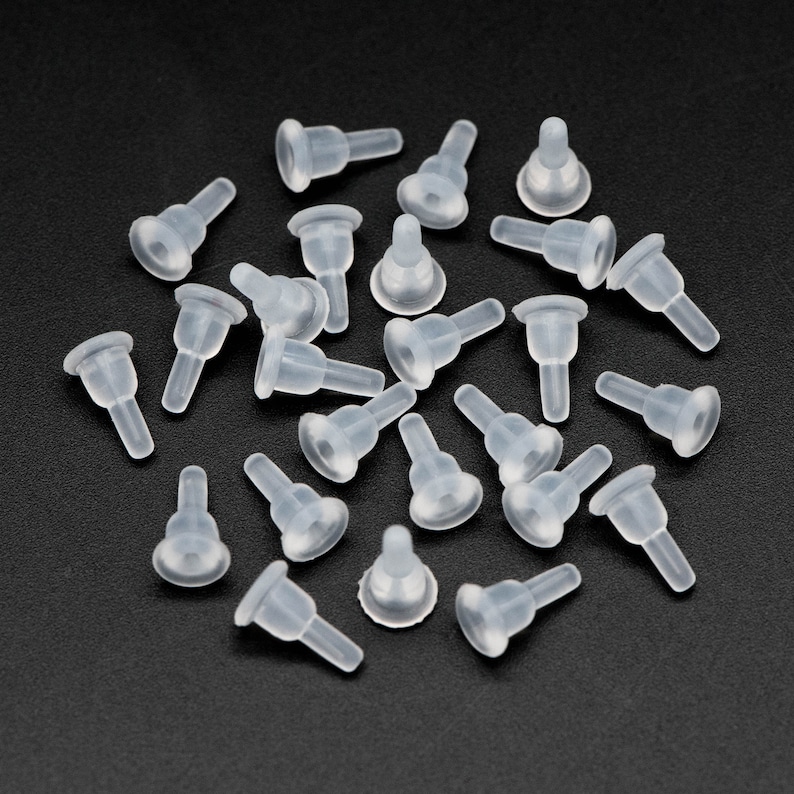May include: A group of 25 clear plastic bottle stoppers with a small, round, pointed tip. The stoppers are scattered on a black surface.
