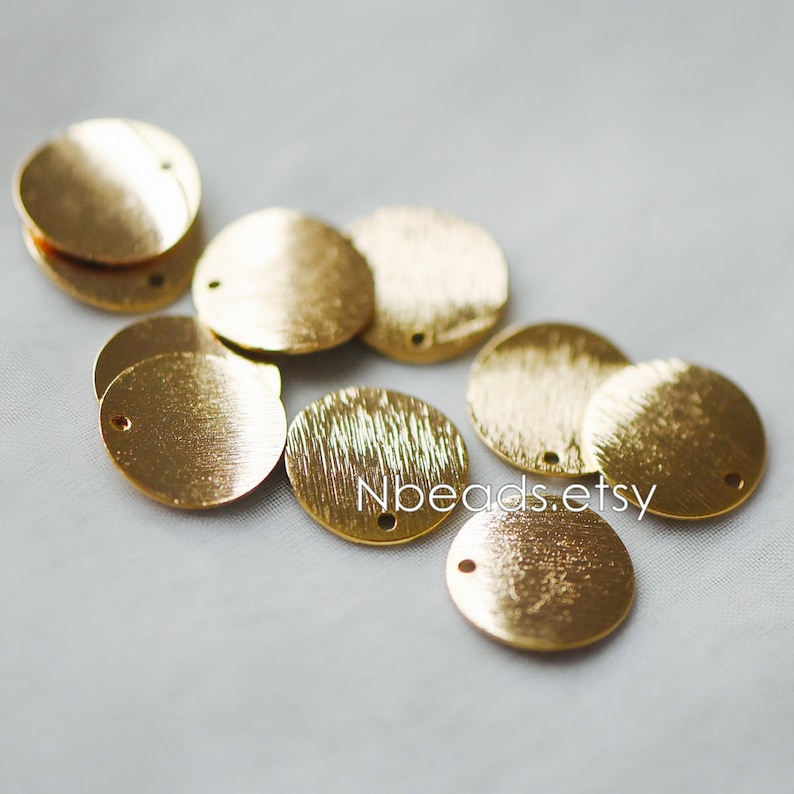 May include: A group of ten gold-colored metal round discs with a hole in the center. The discs have a brushed finish and are arranged in a random pattern.