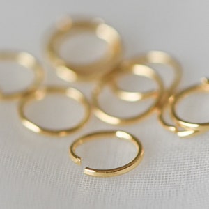 May include: A group of eight gold jump rings, some are stacked on top of each other. The jump rings are a popular jewelry making supply.
