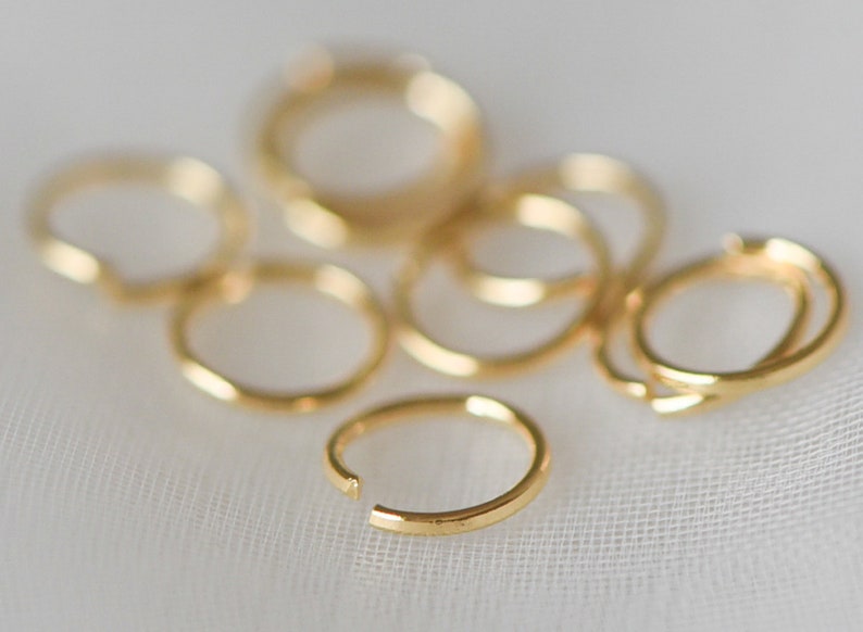 May include: A group of eight gold jump rings, some are stacked on top of each other. The jump rings are a popular jewelry making supply.