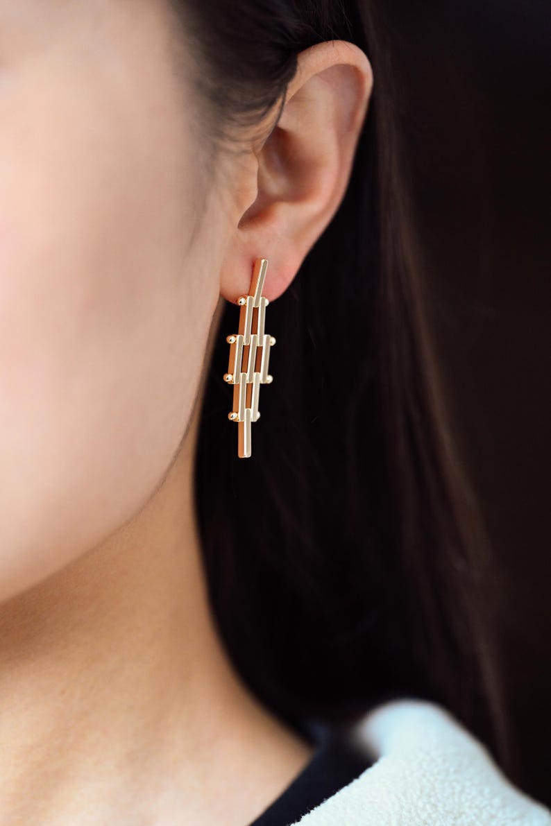 Puede incluir: Pendientes geom&eacute;tricos dorados con un dise&ntilde;o largo y delgado. Los pendientes est&aacute;n hechos de varias barras conectadas con peque&ntilde;os acentos redondos.