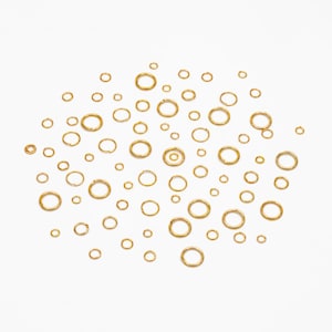 May include: A collection of gold jump rings of various sizes scattered on a white background.