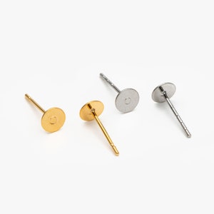 Könnte beinhalten: Drei Ohrstecker mit flachen, runden Oberseiten. Ein Stecker ist golden, zwei Stecker sind silber.