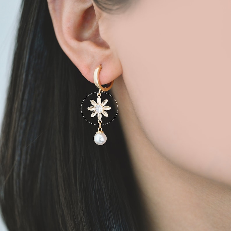 May include: Gold hoop earrings with a dangling pearl and a small flower charm with clear stones.