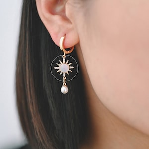 May include: Gold hoop earrings with a pearl drop and a sun-shaped charm with a white mother-of-pearl centre and clear crystal accents.